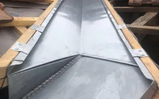 Noue en zinc se déversant dans un chéneau de rive en pied avec un raccord mural biais en tête